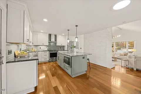 a kitchen with stainless steel appliances granite countertop a stove top oven a sink dishwasher and white cabinets with wooden floor