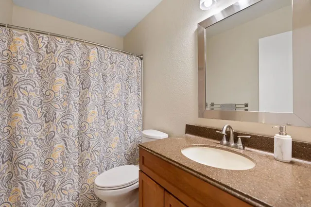 a bathroom with a granite countertop sink a toilet and a mirror