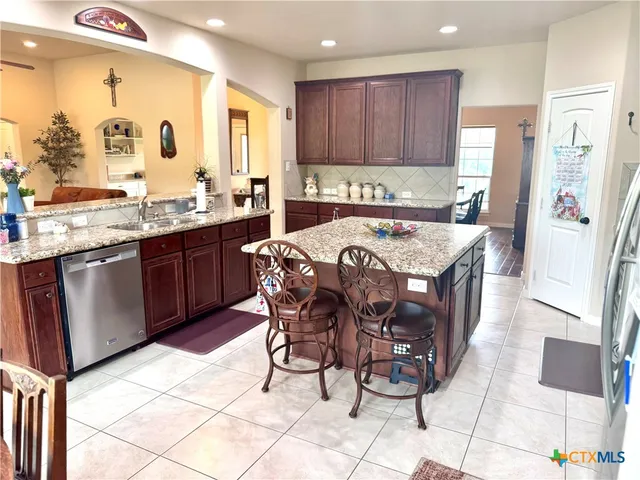 a kitchen with stainless steel appliances granite countertop a sink a stove a refrigerator and island with wooden cabinets