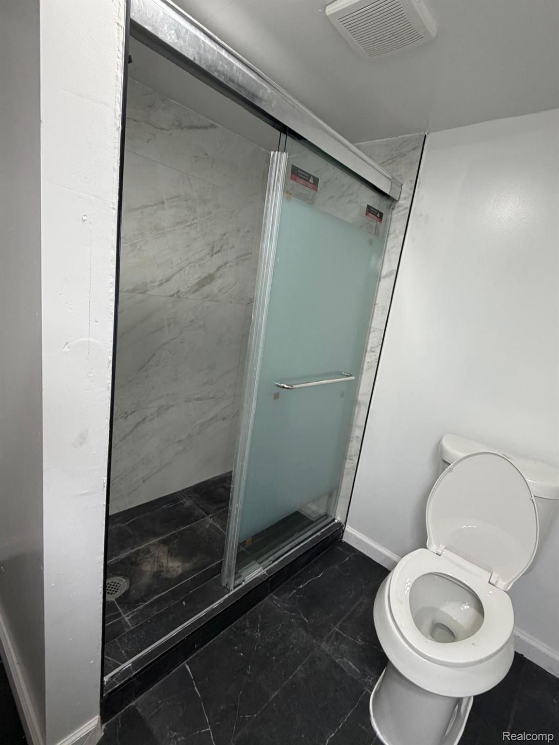 10441 Roxbury Street Detroit, MI 48224 - Photo 22 of 22 Shower enclosure with sliding frosted glass door, white marbled wall tiling, and dark stone-finish flooring
