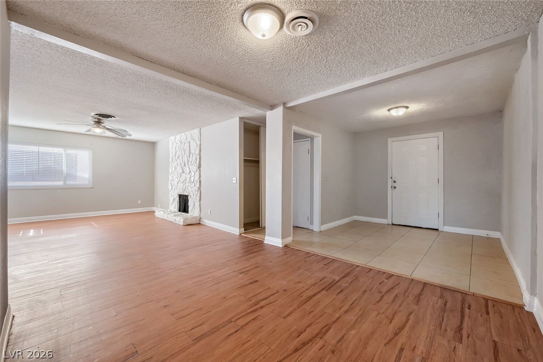 6321 Portola Road Las Vegas, NV 89108 - Photo 5 of 29 A comfortable living space featuring a textured stone fireplace, wood floors, and a ceiling fan for year-round comfort.