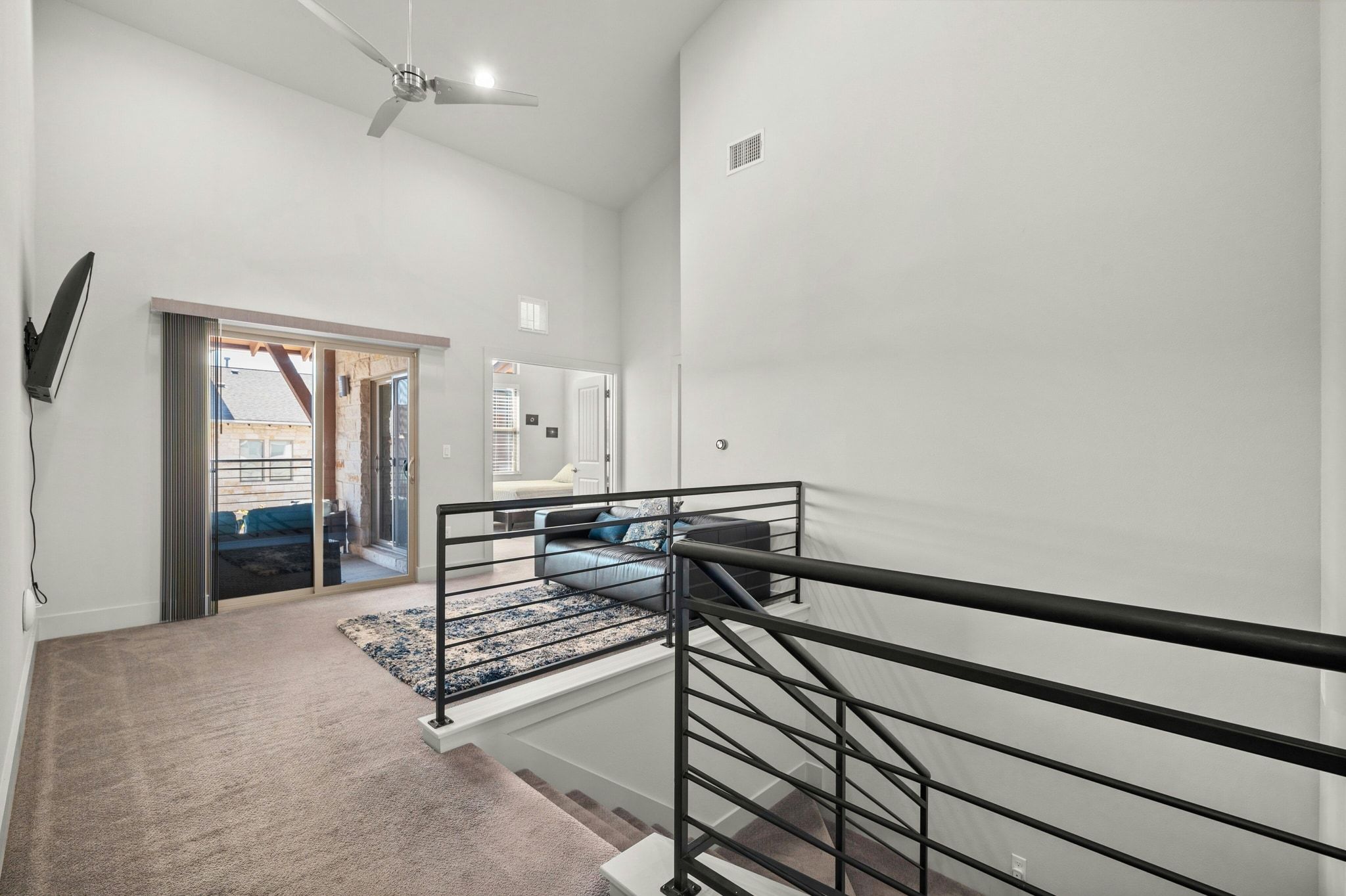 8110 Ranch Road 2222, Unit 92 Austin, TX 78730 - Photo 19 of 40 Carpeted loft area featuring a vaulted ceiling with a ceiling fan, a sliding glass door opening to an outdoor patio, and modern black metal railings overlooking a lower level