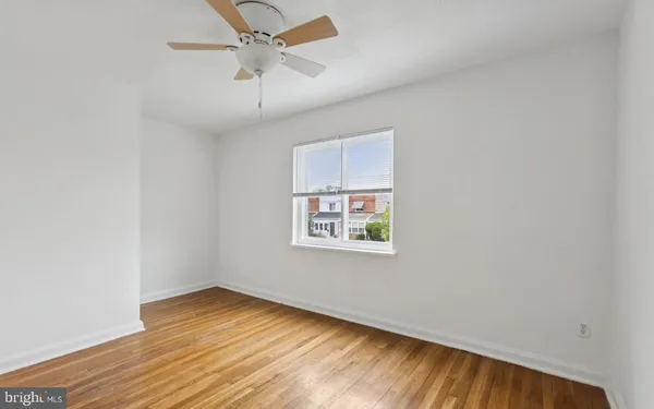 an empty room with wooden floor ceiling fan and windows