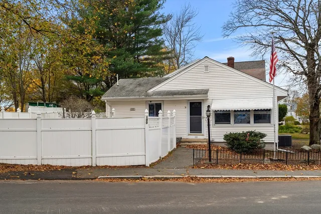 a view of a white house with a large tree and wooden fence