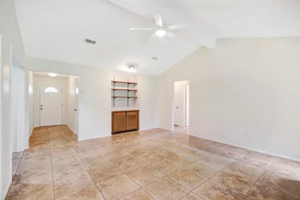 an empty room with kitchen view and a ceiling fan