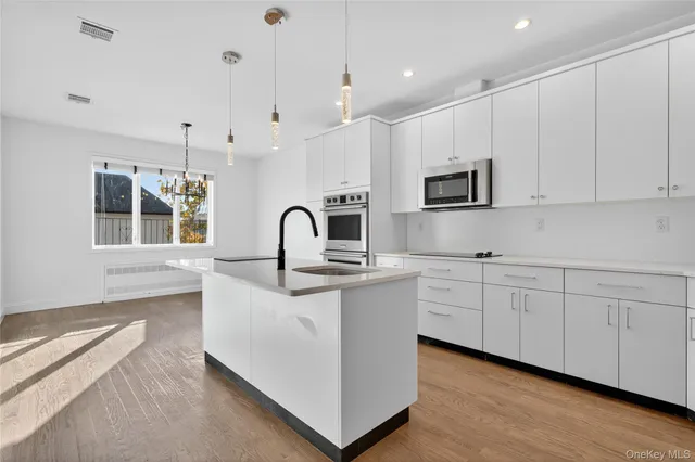 a kitchen with stainless steel appliances granite countertop a stove a sink a refrigerator and white cabinets with wooden floor