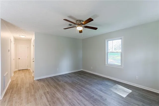 a view of empty room with wooden floor and fan