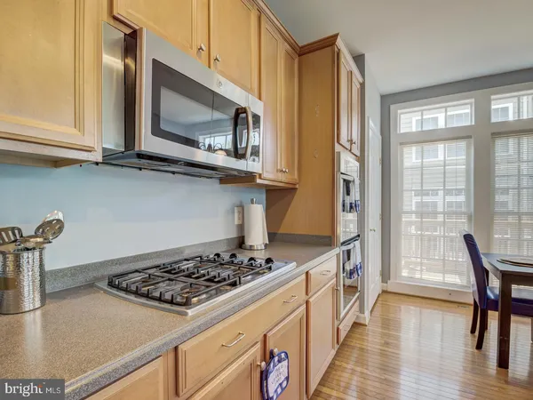 a kitchen with stainless steel appliances granite countertop a refrigerator a sink dishwasher a stove and a dining table with wooden floor