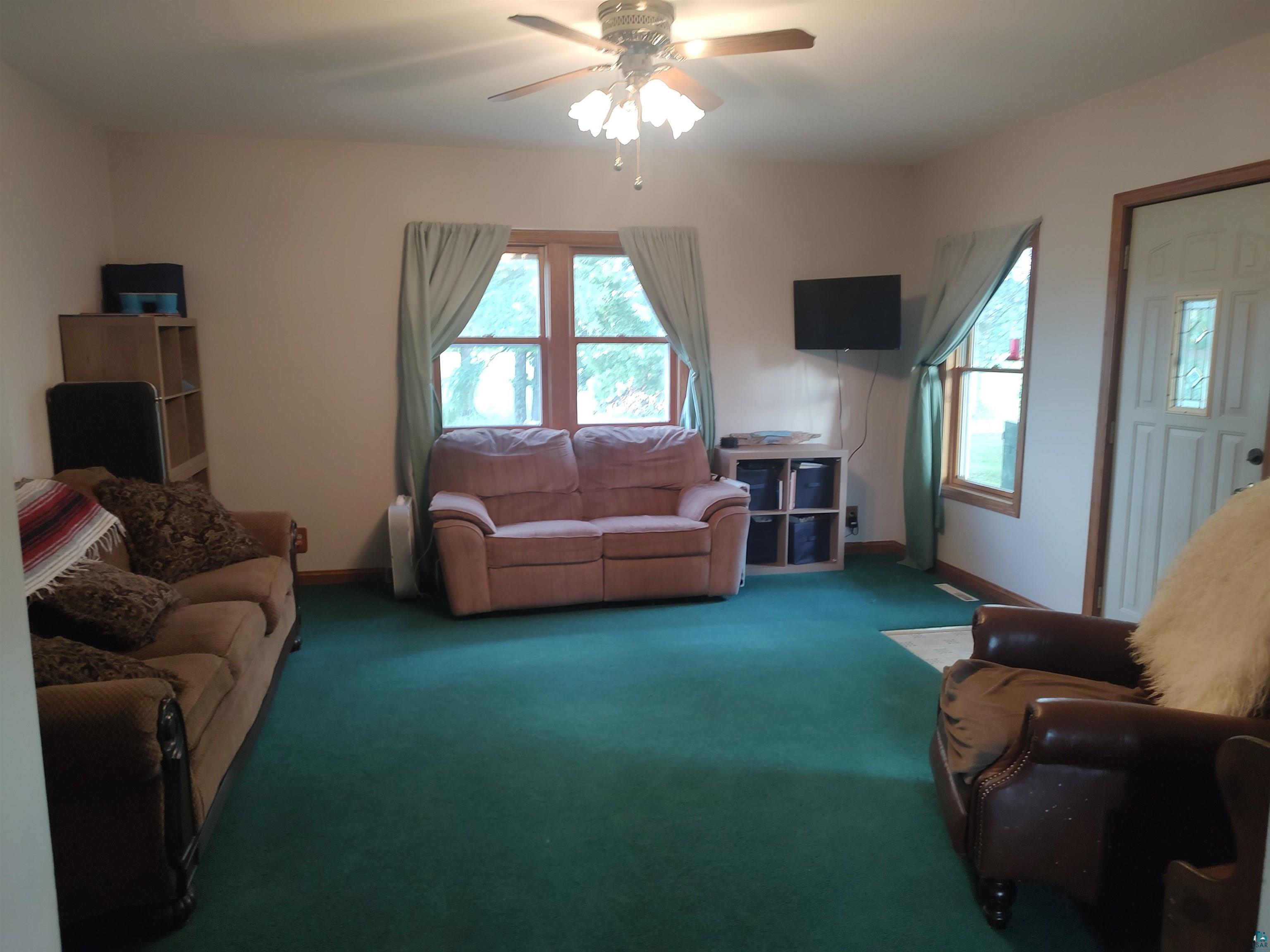 2585 Hautala Road Iron River, WI 54847 - Photo 6 of 28 Living area featuring green carpeting, a ceiling fan with integrated lighting, and multiple windows with wood trim