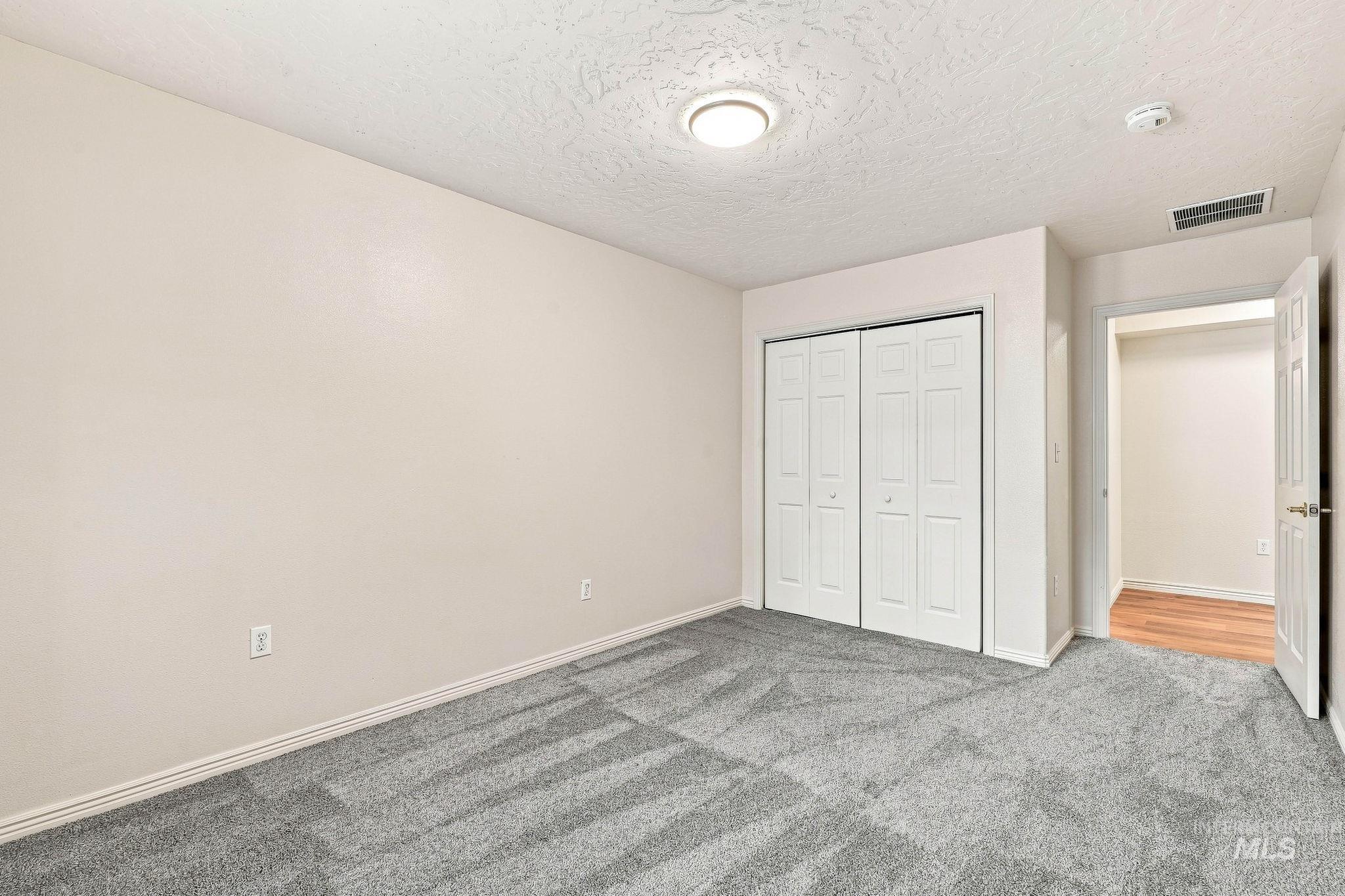 2442 West Hill Road Boise, ID 83702 - Photo 32 of 48 Neutral wall paint, textured ceiling, flush mount lighting, white bi-fold closet doors, and gray patterned carpeting