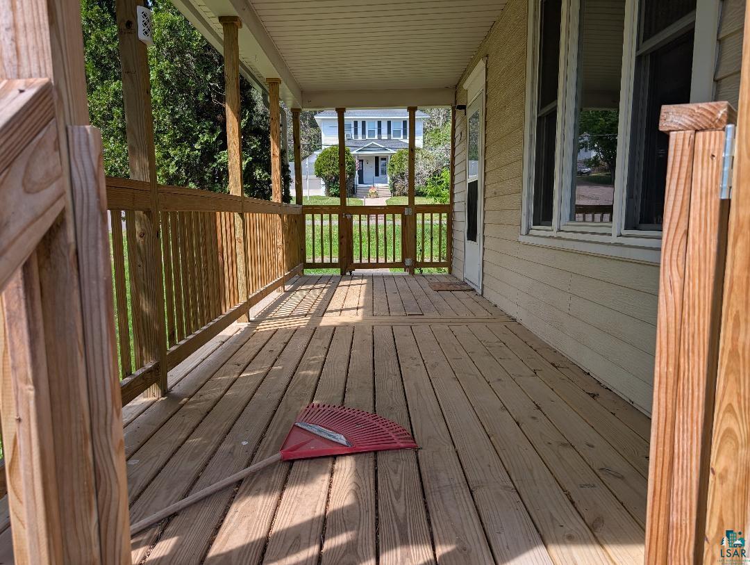 202 Thomas Street Mellen, WI 54546 - Photo 6 of 6 Inviting covered porch with natural wood railing and flooring, featuring a light-colored siding exterior and multiple windows