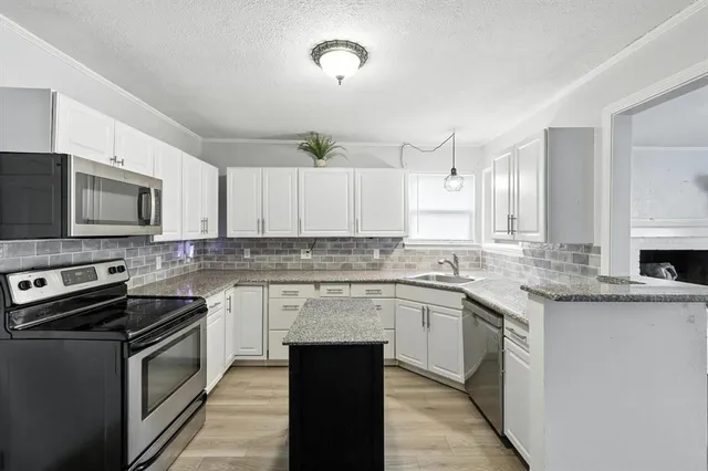 a kitchen with stainless steel appliances granite countertop a stove top oven a sink dishwasher and a microwave oven with white cabinets