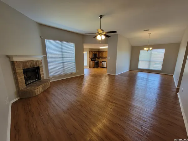 an empty room with wooden floor fireplace and kitchen view