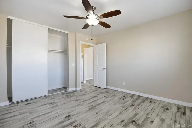 an empty room with wooden floor ceiling fan and windows