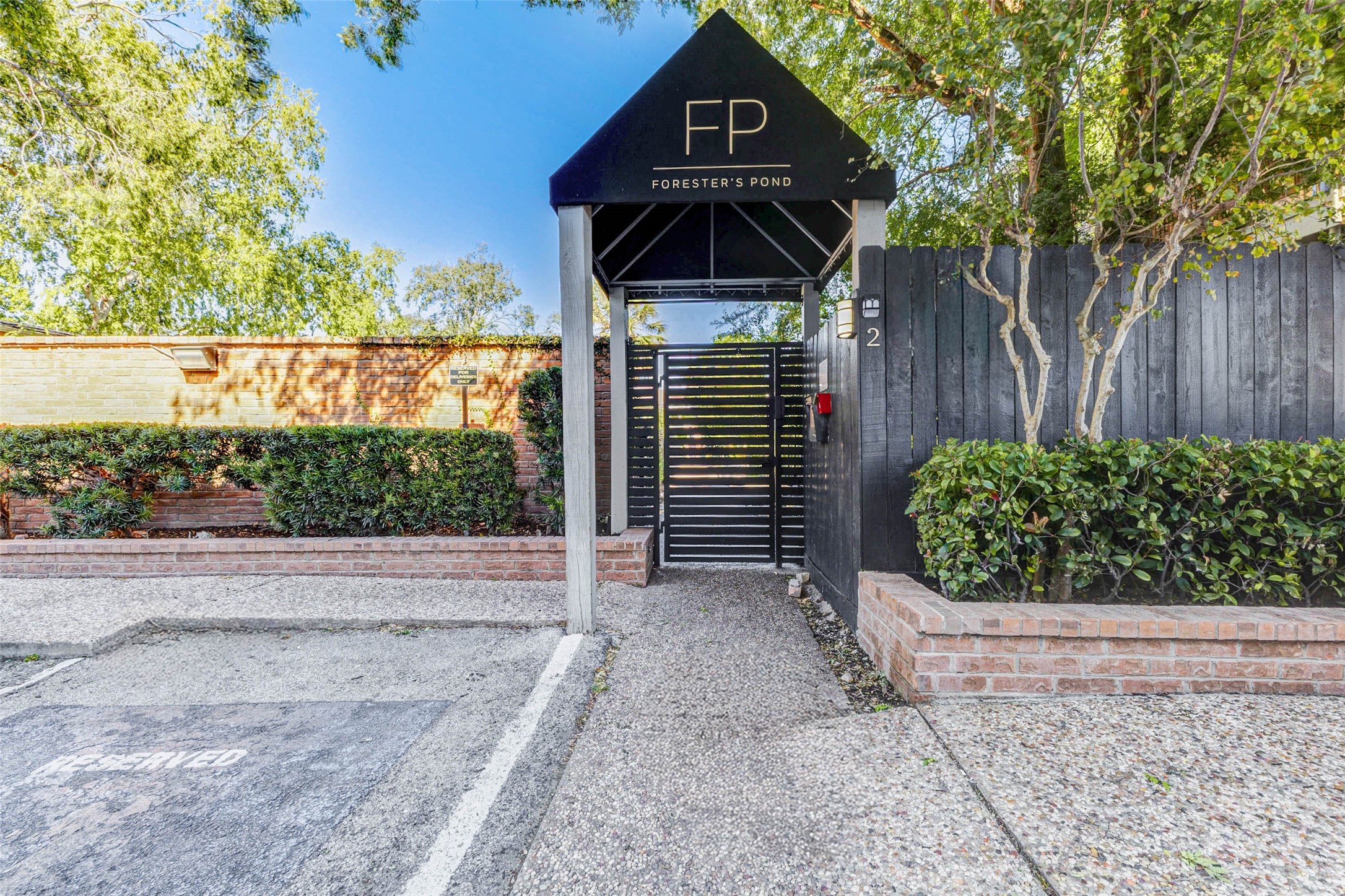 3928 West Alabama Street, Unit 4 Houston, TX 77027 - Photo 11 of 33 Residential community named "Forrester's Pond." The entrance features a modern black gate with a canopy, lined with greenery and brick accents, conveying a welcoming and secure environment.