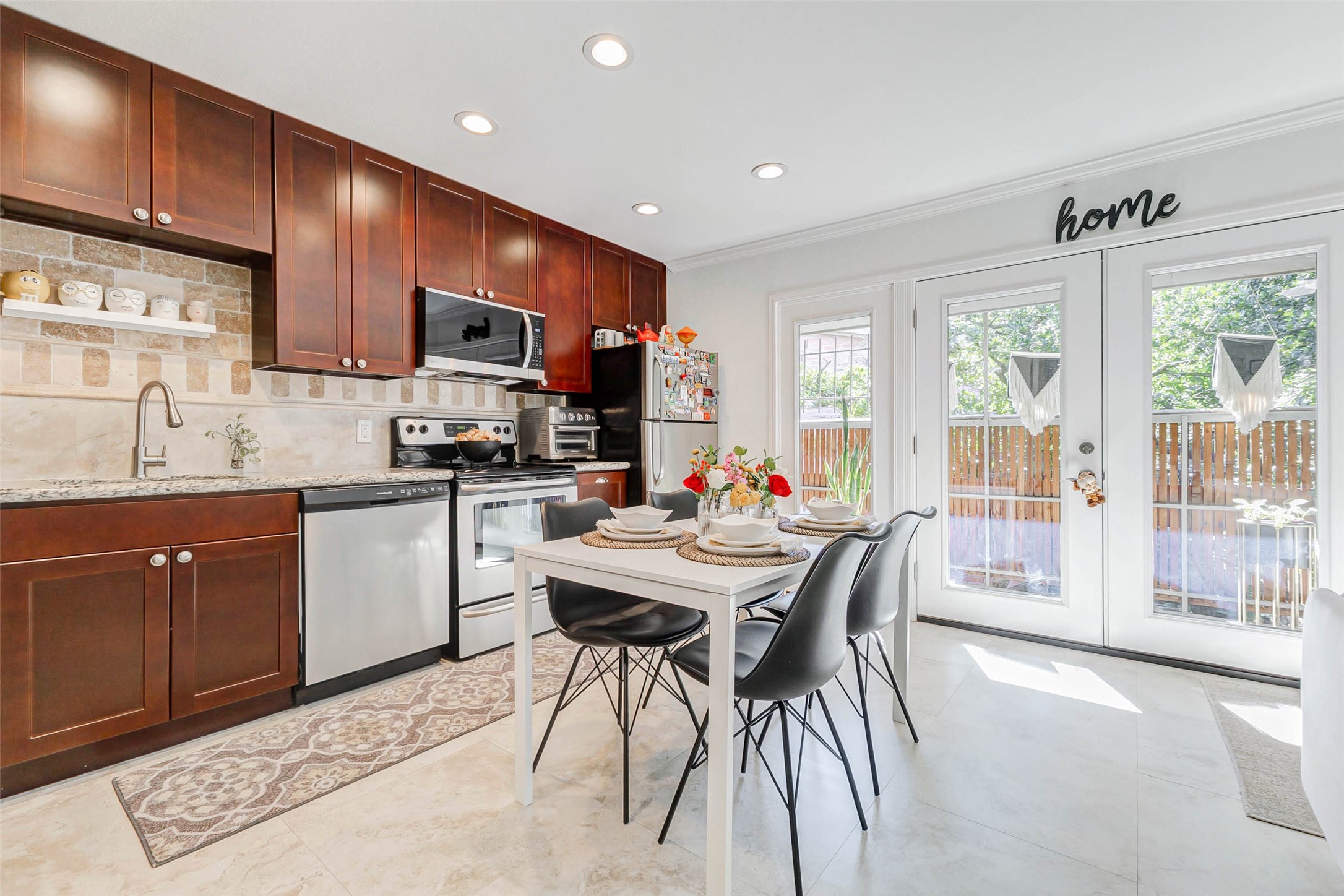 3928 West Alabama Street, Unit 4 Houston, TX 77027 - Photo 4 of 33 This bright kitchen features sleek stainless steel appliances, rich wood cabinetry, and a cozy dining area. French doors open to a serene view, allowing natural light to fill the space. Ideal for enjoying meals and entertaining.