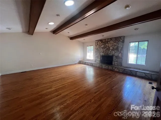 an empty room with wooden floor fireplace and windows