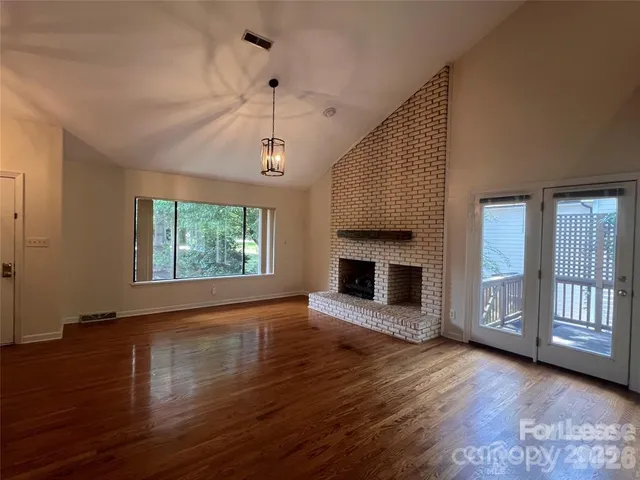 an empty room with wooden floor fireplace and windows