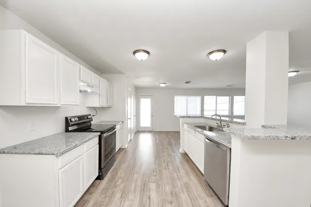 a kitchen with stainless steel appliances granite countertop a stove a sink a refrigerator and white cabinets with wooden floor