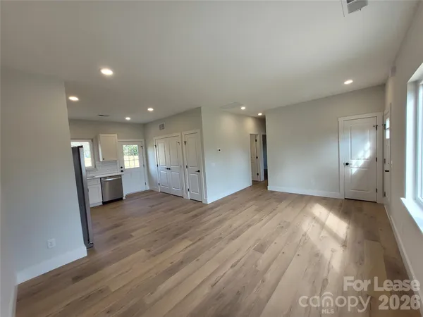 a view of empty room with wooden floor and kitchen