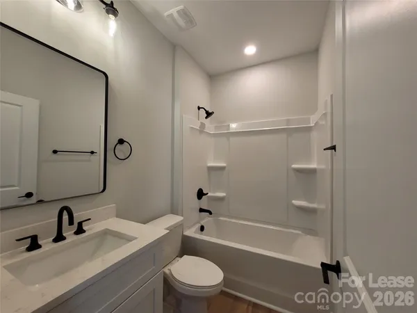 a bathroom with a bathtub shower sink vanity mirror and toilet