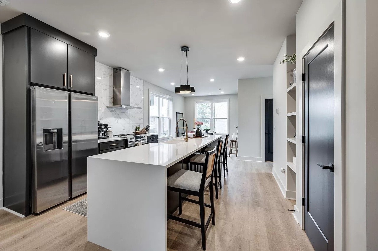 a kitchen with stainless steel appliances kitchen island granite countertop a refrigerator a sink dishwasher a stove and a refrigerator with wooden floor