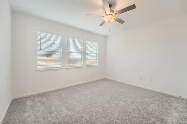 an empty room with chandelier fan and windows