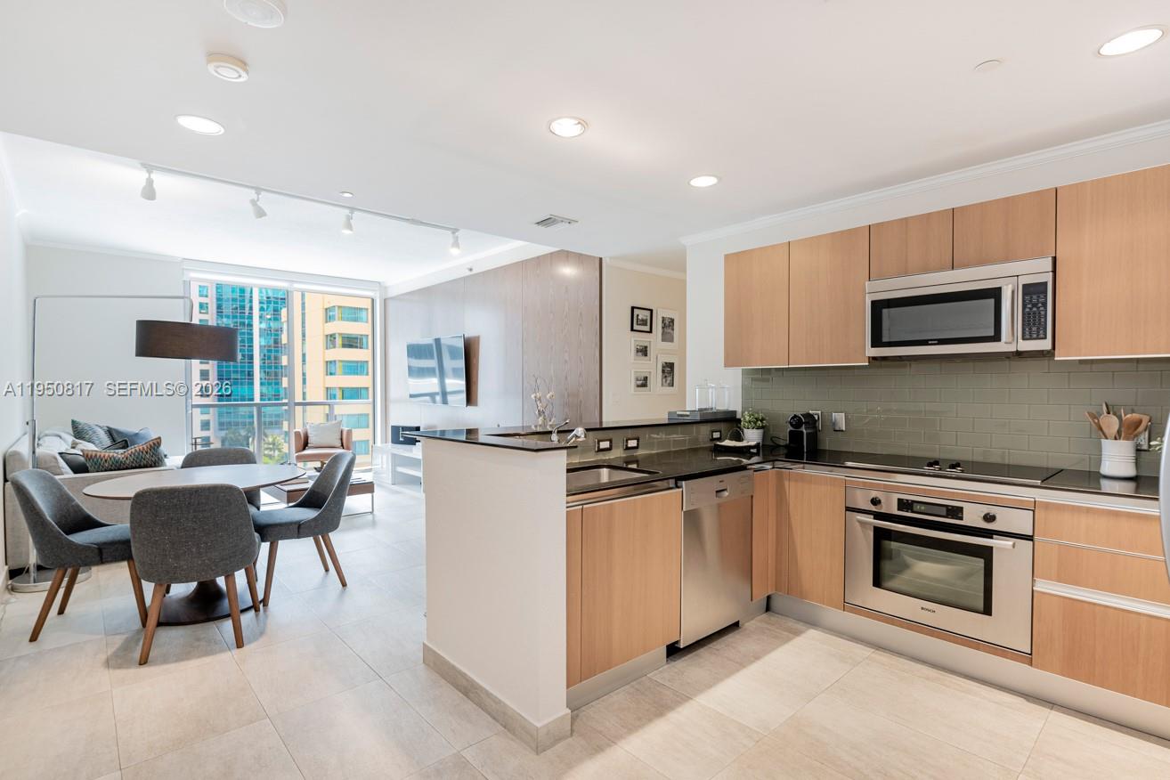 1060 Brickell Avenue, Unit 1507 Miami, FL 33131 - Photo 25 of 56 a kitchen with stainless steel appliances granite countertop a stove top oven a sink dishwasher a dining table and chairs with wooden floor