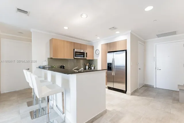 a kitchen with stainless steel appliances kitchen island granite countertop a dining table chairs and a refrigerator