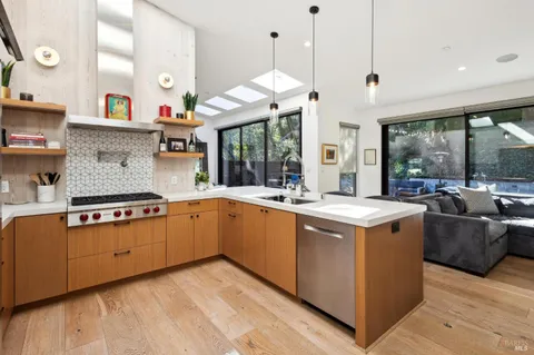 a kitchen with stainless steel appliances a white stove top oven a sink a dining table and chairs with wooden floor