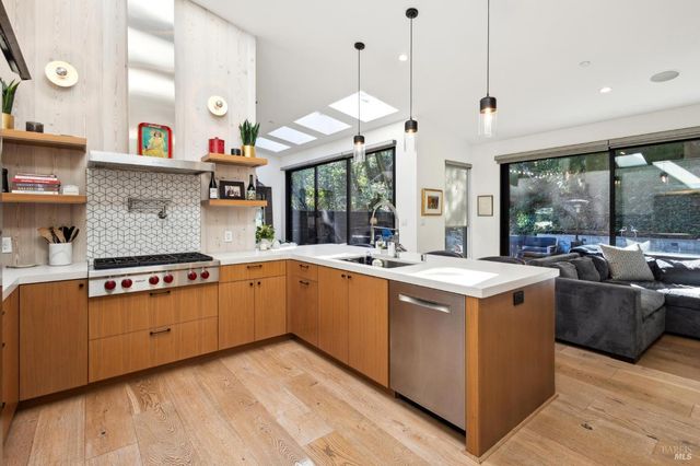 a kitchen with stainless steel appliances a white stove top oven a sink a dining table and chairs with wooden floor