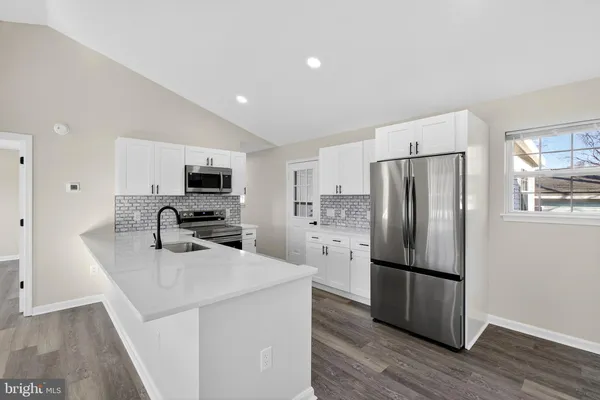 a kitchen with stainless steel appliances a sink dishwasher a stove a refrigerator with white cabinets and wooden floor