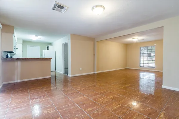 a view of an empty room with kitchen and window