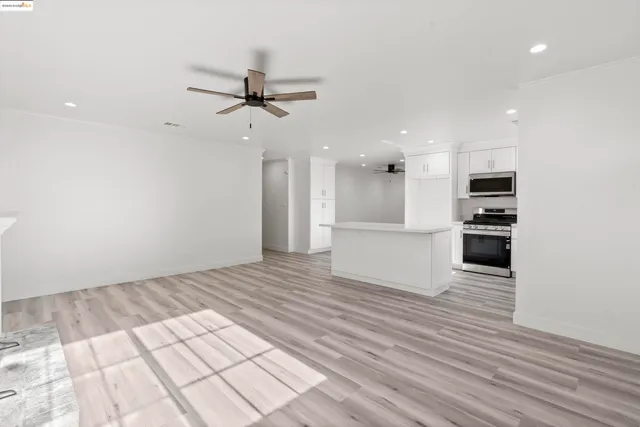 an empty room with wooden floor kitchen view and a window