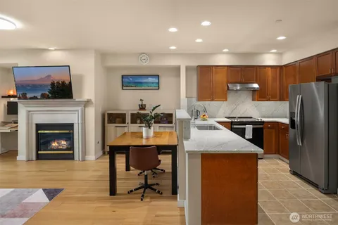 a kitchen with stainless steel appliances granite countertop a refrigerator a stove a sink and a fireplace with wooden floor
