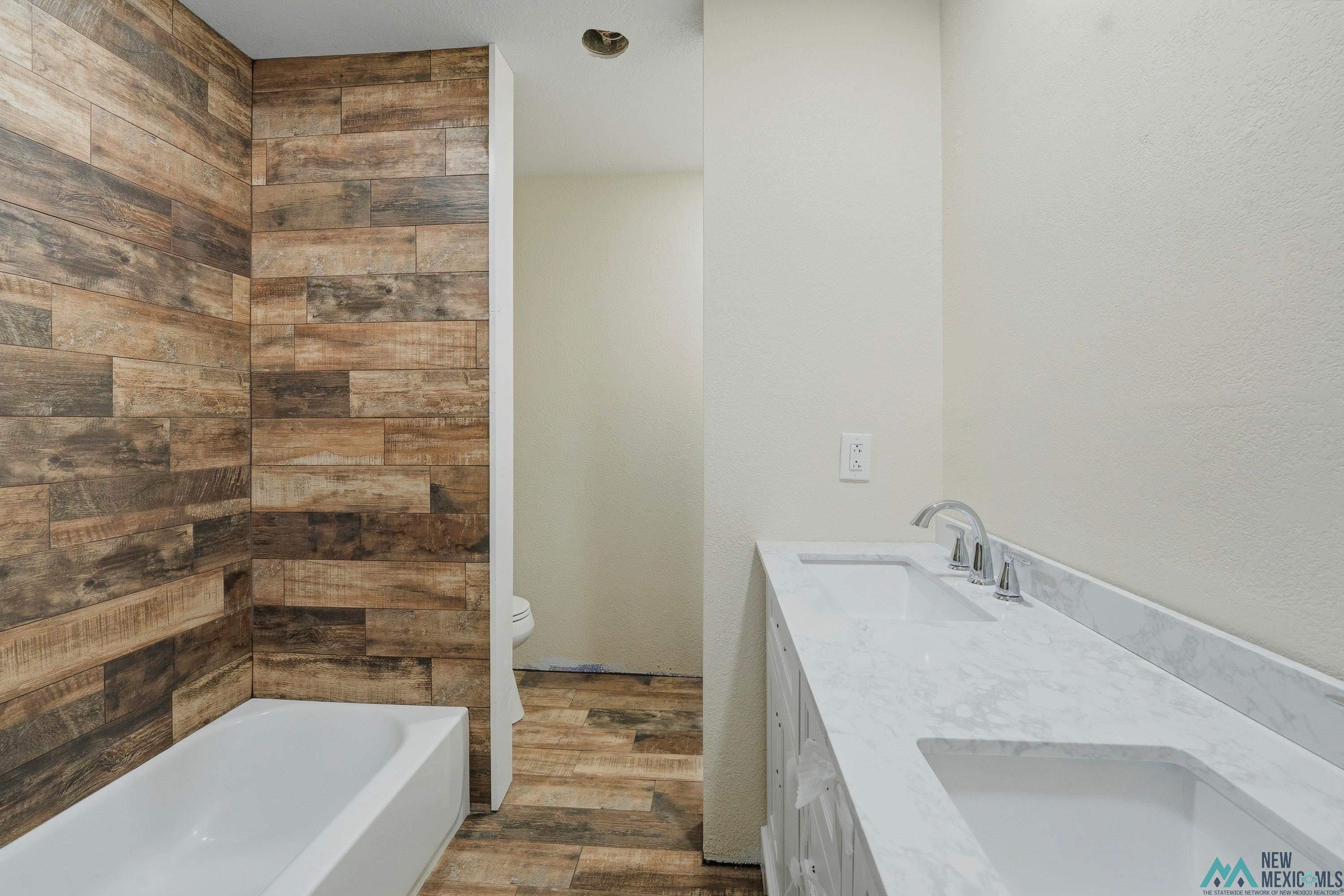544 South 13th Avenue Raton, NM 87740 - Photo 24 of 37 Bathroom featuring a double vanity with integrated sinks, a white bathtub, and wood-finish wall and floor tiling
