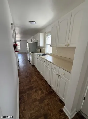 a kitchen with granite countertop a refrigerator a sink and white cabinets
