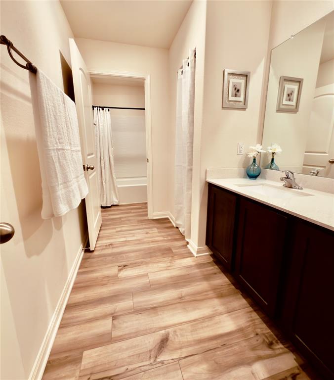 196 Cattlemans Crk Road West Newark, TX 76071 - Photo 16 of 24 Bathroom featuring wood-finish flooring, a dark wood-tone vanity with a light countertop, a rectangular mirror, and a white bathtub with a shower curtain