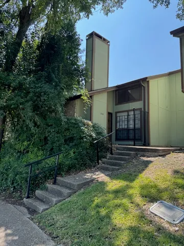 a view of a house with brick walls plants and large tree