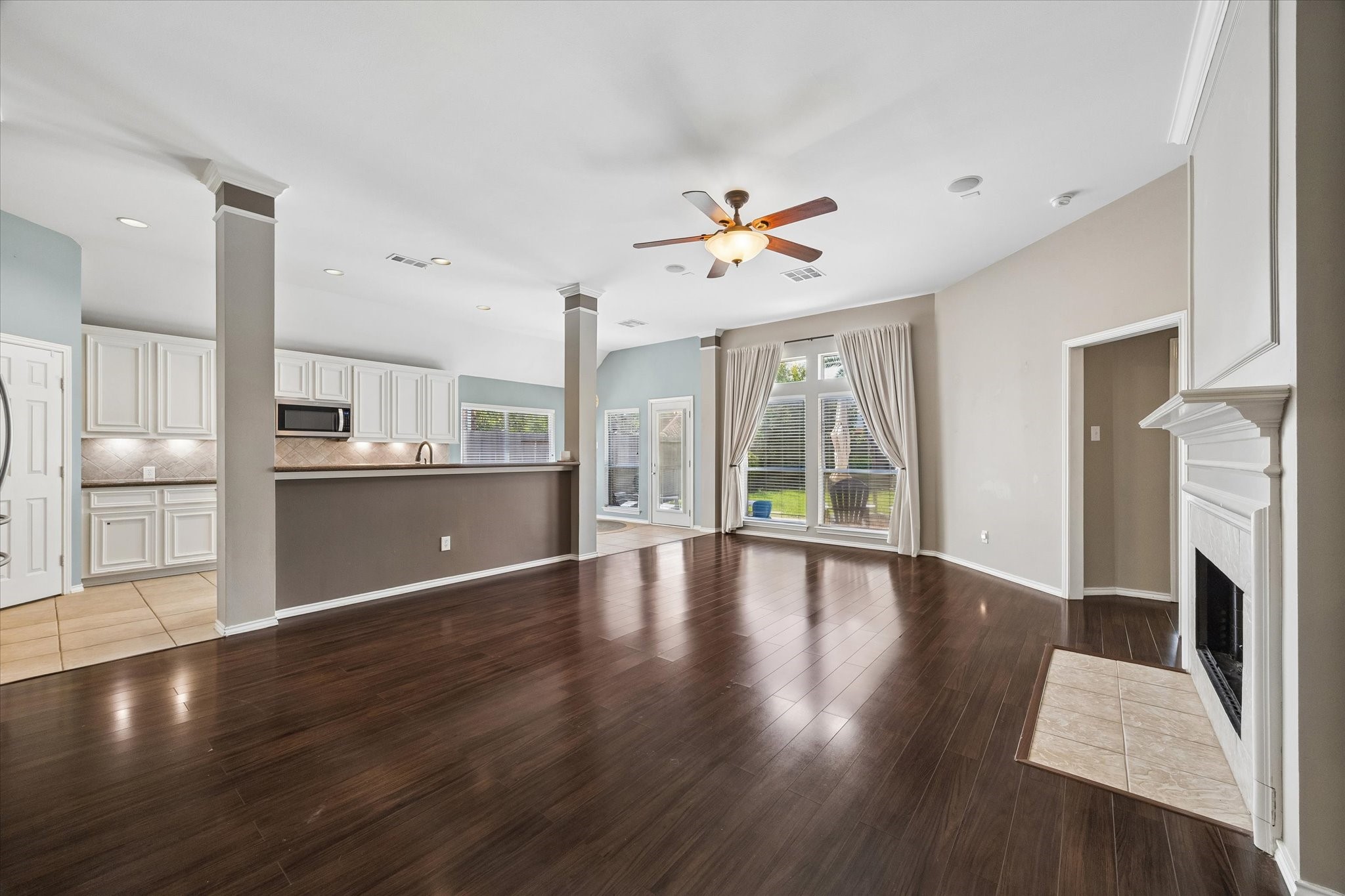 3118 Valley Court Manvel, TX 77578 - Photo 25 of 38 This spacious, open-concept living area features dark hardwood floors, a modern kitchen with white cabinetry and a breakfast bar, a cozy fireplace, and large windows with elegant drapes, offering ample natural light.
