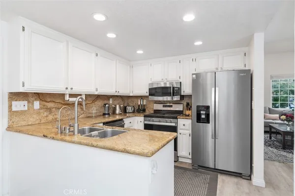 a kitchen with kitchen island granite countertop a refrigerator a stove a sink and white cabinets with wooden floor