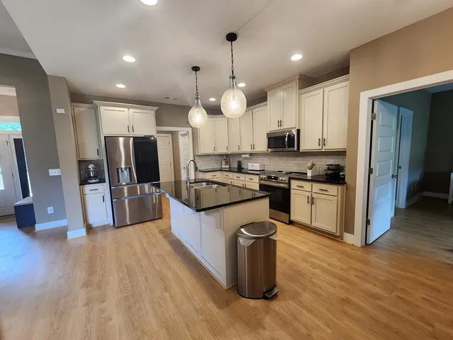 a large kitchen with stainless steel appliances granite countertop a stove a sink dishwasher a refrigerator and white cabinets with wooden floor