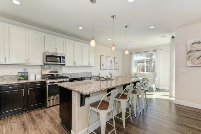 a kitchen with stainless steel appliances granite countertop a stove top oven a sink dishwasher a dining table and chairs with wooden floor