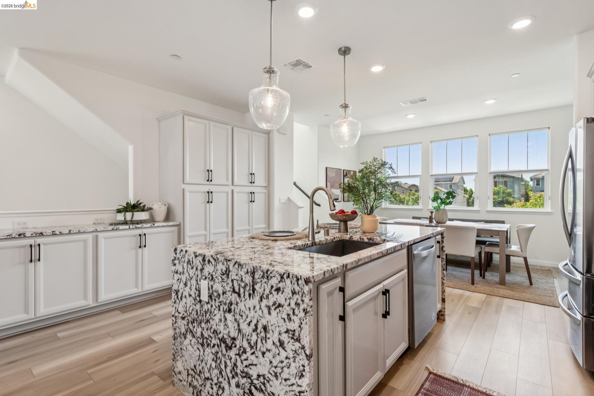 24157 Amaranth Loop Hayward, CA 94541 - Photo 22 of 63 Kitchen featuring a large central island with a stone countertop and integrated sink, light wood-finish flooring, white cabinetry with black hardware, recessed lighting, and multiple windows