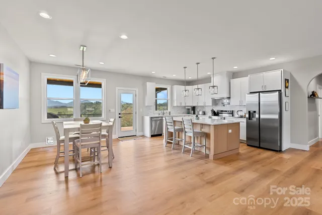 a kitchen with stainless steel appliances kitchen island granite countertop a refrigerator a stove a dining table and chairs with wooden floor