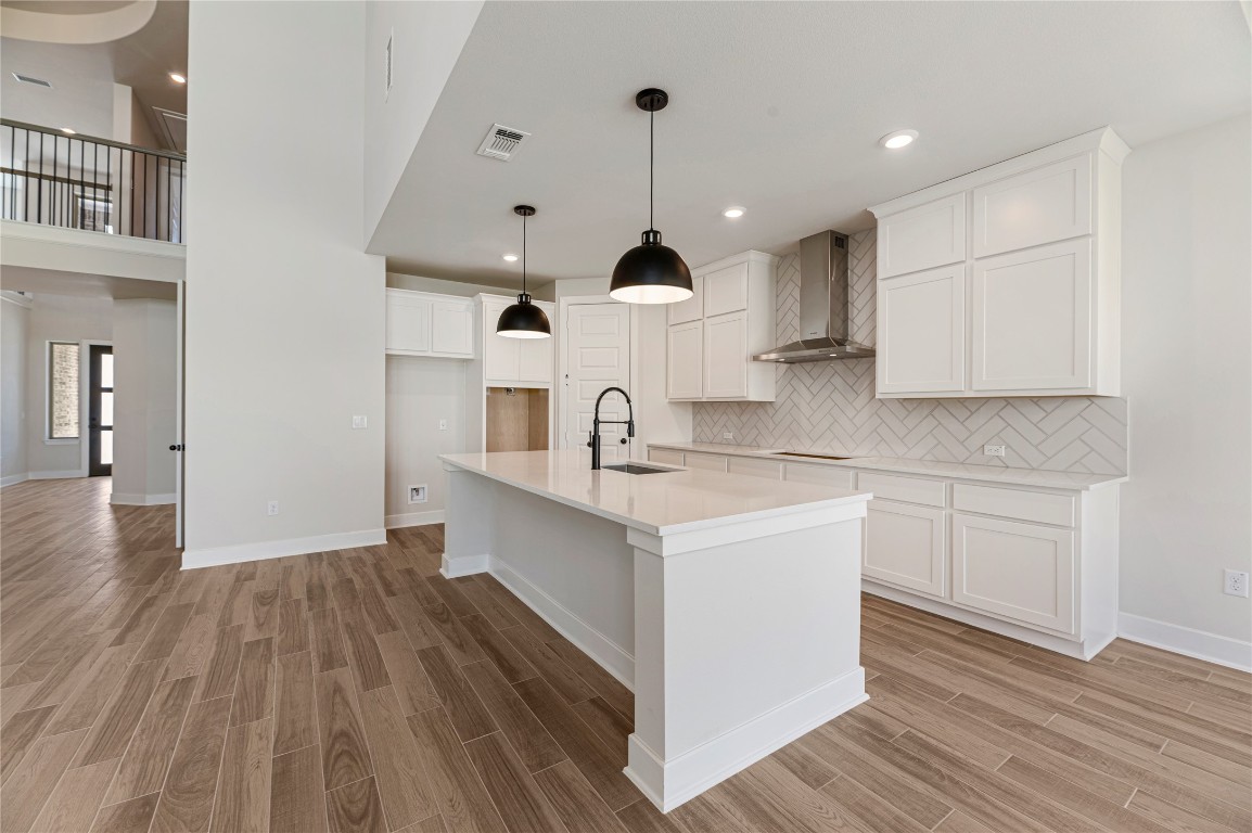 1508 Rodeo Ridge Drive Georgetown, TX 78628 - Photo 6 of 37 Kitchen featuring tasteful backsplash, a kitchen island with sink, a kitchen bar, wall chimney range hood, and pendant lighting
