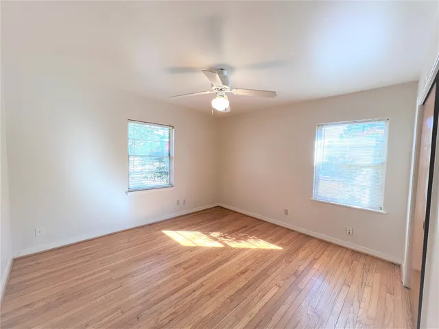 an empty room with wooden floor chandelier fan and windows