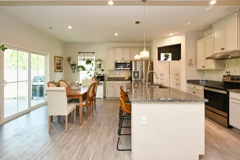 a kitchen with stainless steel appliances granite countertop a stove top oven a sink a dining table and chairs