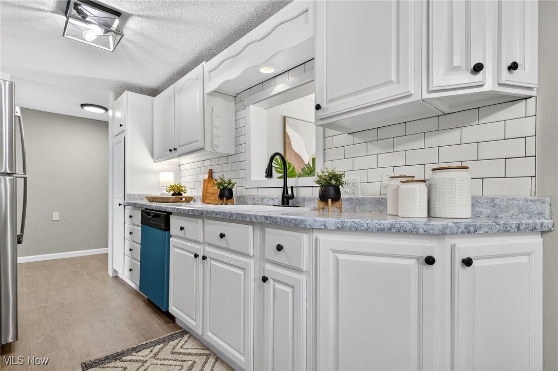 8230 Drake State Line Road Masury, OH 44438 - Photo 18 of 47 Kitchen with white cabinetry, light wood-type flooring, tasteful backsplash, freestanding refrigerator, and dishwasher