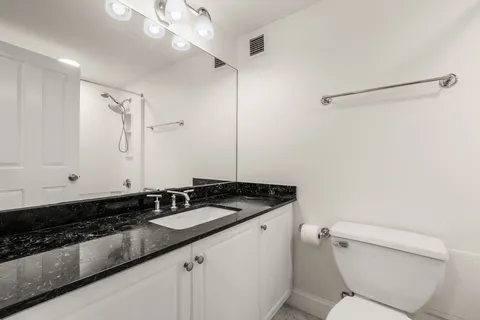 a bathroom with a granite countertop sink a toilet a mirror and shower
